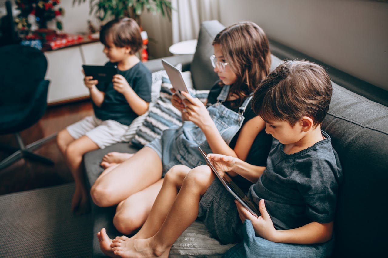 Three children sitting on a couch with a tablet